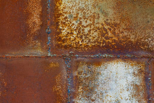 Close up of a brownish rusted welded sheet metal surface with yellowish and orange hue and amber patina.
