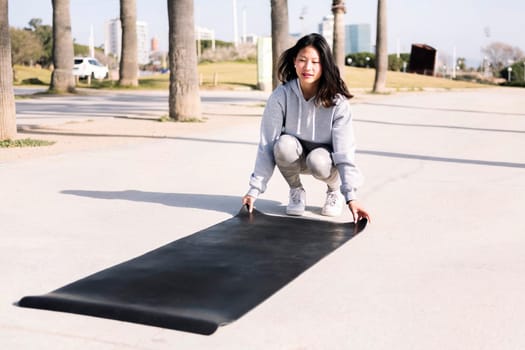 young asian woman dressed in sportswear placing her mat for a yoga session outdoors, healthy and active lifestyle concept,