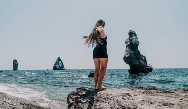 Woman travel sea. Young Happy woman in a long red dress posing on a beach near the sea on background of volcanic rocks, like in Iceland, sharing travel adventure journey