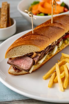 Grilled steak sandwich with french fries on a white porcelain plate