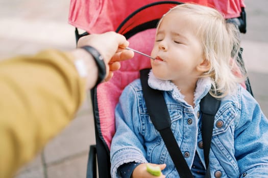 Little girl, closing her eyes, eats from the spoon that her dad feeds her. High quality photo