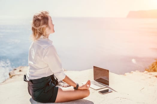 Happy girl doing yoga with laptop working at the beach. beautiful and calm business woman sitting with a laptop in a summer cafe in the lotus position meditating and relaxing. freelance girl remote work beach paradise