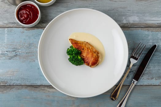 Grilled chicken breast with broccoli and sauce on a white porcelain plate