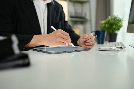 Close up male economist in black suit using digital tablet on white office desk.