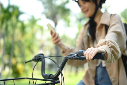 Cropped shot of smiling young woman using mobile phone while sitting on a bicycle.