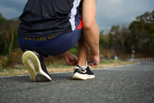 Athlete man tying shoelace getting ready for training outdoor. Healthy lifestyle concept.