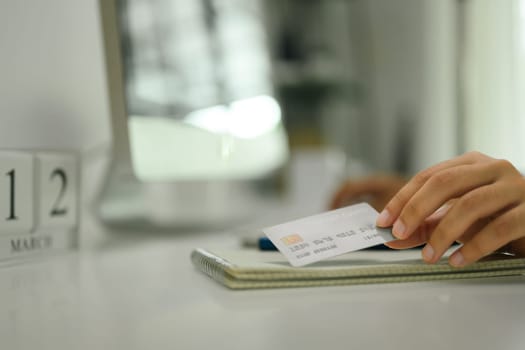 Woman holding credit card sitting at office desk. Online internet banking concept.