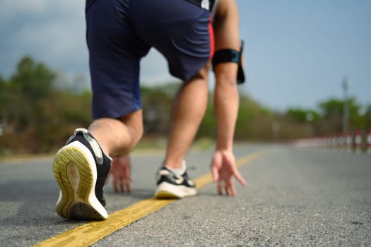 Unrecognizable athlete in start position ready to run on road.