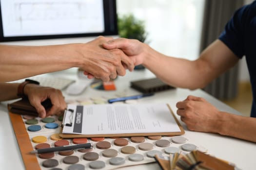 Interior designer and client shaking hands after signing agreement at office.