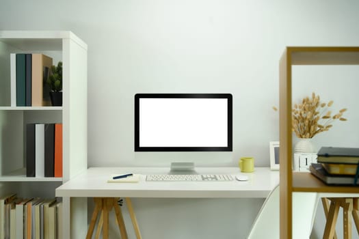 Front view of blank computer screen on white table in modern home office.