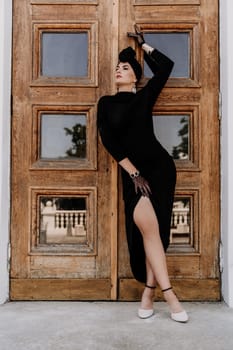 Stylish woman in the city. Fashion photo of a beautiful model in an elegant black dress posing against the backdrop of a building on a city street.