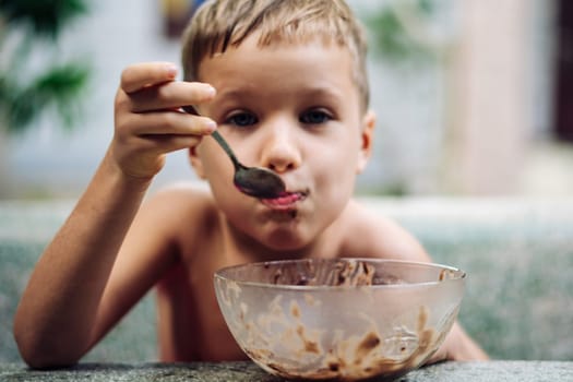 Happy childhood. Boy eating fruits with cacao spoon, summer day outside. Cute lover of sweets and tasty things .