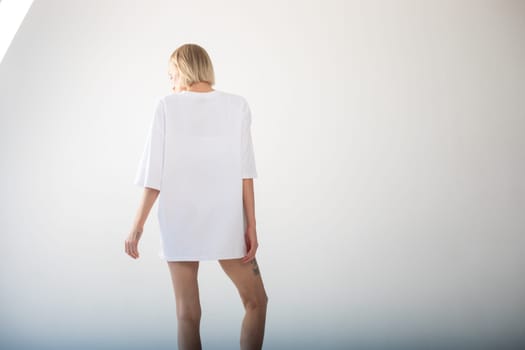 Beautiful girl in a white oversized t-shirt posing on a white background. High quality photo