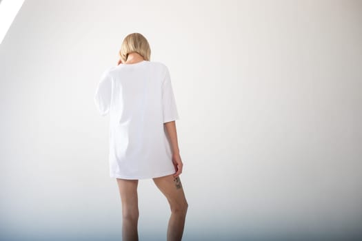 Beautiful girl in a white oversized t-shirt posing on a white background. High quality photo