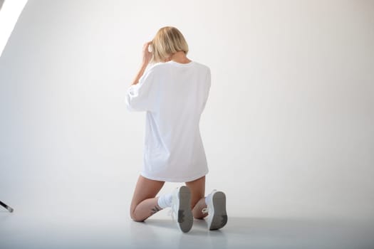 Beautiful girl in a white oversized t-shirt posing on a white background. High quality photo