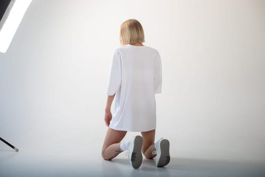 Beautiful girl in a white oversized t-shirt posing on a white background. High quality photo