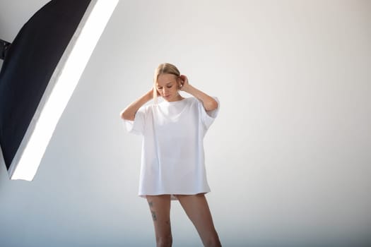 Beautiful girl in a white oversized t-shirt posing on a white background. High quality photo