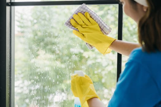 Maid wearing gloves cheerfully cleans office windows with a spray and cloth. Her dedication to housework emphasizes purity hygiene and transparent cleanliness.