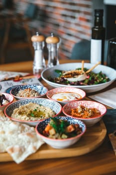 An assortment of Mediterranean mezze dishes served with fresh vegetables, hummus, and pita bread on a wooden board.