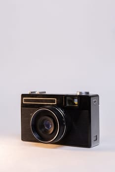 A black vintage camera with a lens is isolated on a white background with a spotlight on the front right side of the camera.