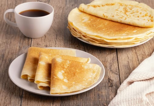 Stack of Russian thin pancakes and coffee on a wooden table.