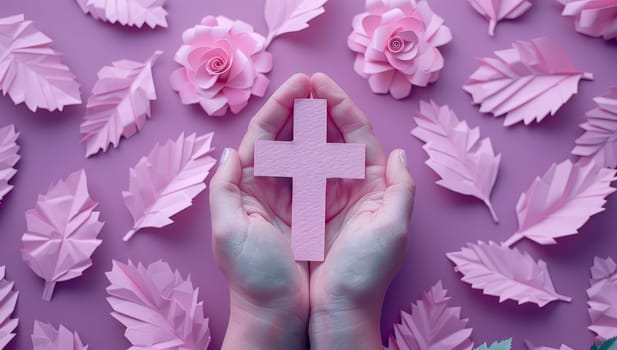 Female hands holding a pink christian cross surrounded by pink paper flowers.