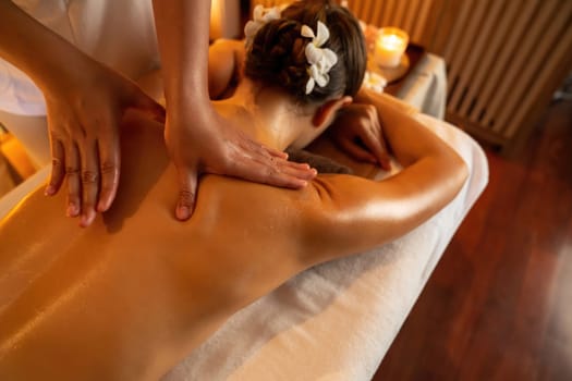 Caucasian woman customer enjoying relaxing anti-stress spa massage and pampering with beauty skin recreation leisure in warm candle lighting ambient salon spa at luxury resort or hotel. Quiescent