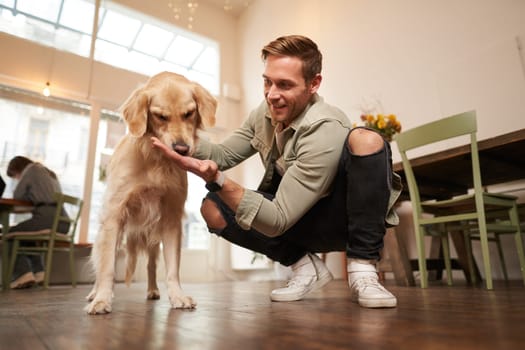 Close up portrait of happy dog owner, man with his pet giving a treat, spending time in animal-friendly cafe or co-working space.