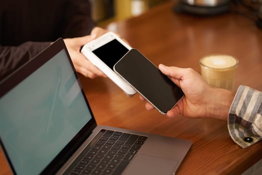 Cropped shot of hand pressing phone to POS paying terminal to pay contactless for an order, using smartphone to make purchase in cafe or co-working.