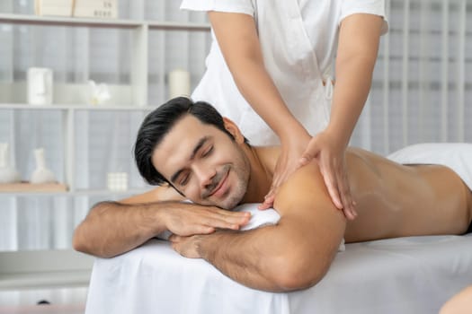 Caucasian man customer enjoying relaxing anti-stress spa massage and pampering with beauty skin recreation leisure in day light ambient salon spa at luxury resort or hotel. Quiescent