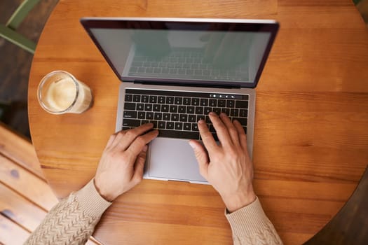 Portrait of male hands, laptop and cappuccino. Man typing on keyboard, working in cafe and drinking coffee, close up of computer screen and arms.