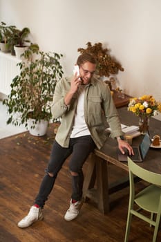 Portrait of a man in office, businessman making a phone call, having a conversation over the phone, receive a call, standing in office, leaning on table.