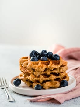 Easy healthy gluten free oat waffles with copy space. Stack of appetizing homemade waffles with oat flour decorated blueberries, on plate over light gray cement background. Vertical