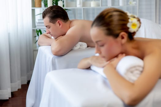 Caucasian couple customer enjoying relaxing anti-stress spa massage and pampering with beauty skin recreation leisure in day light ambient salon spa at luxury resort or hotel. Quiescent