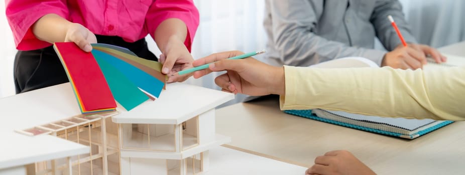 Cropped image of skilled architect and interior designer team collaborate to select house color theme at meeting room with house model placed on table. Creative working and design concept. Variegated.