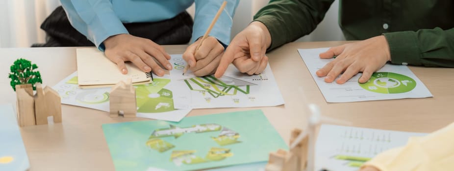 A cropped picture of green city poster was placed at green business meeting on meeting table with environmental document, wooden house block and windmill model scattered around. Closeup. Delineation.