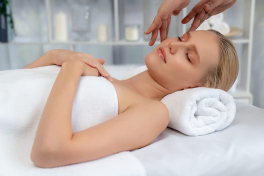 Caucasian woman enjoying relaxing anti-stress head massage and pampering facial beauty skin recreation leisure in dayspa modern light ambient at luxury resort or hotel spa salon. Quiescent