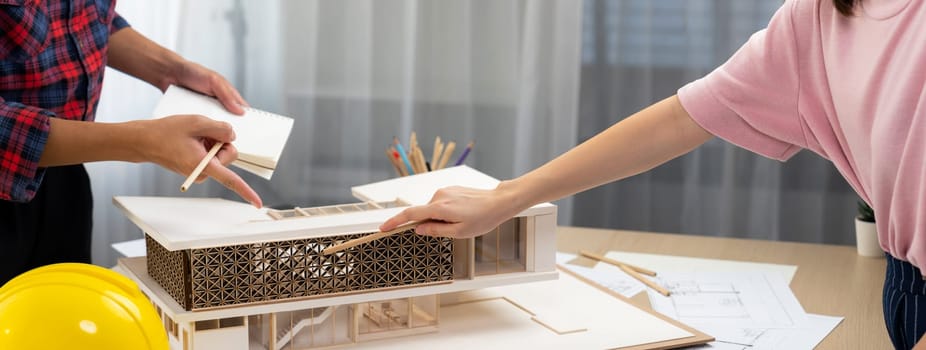 Smart architect engineer and interior designer working together and measuring house model by using ruler on meeting table with blueprint and architectural equipment. Teamwork concept. Burgeoning.