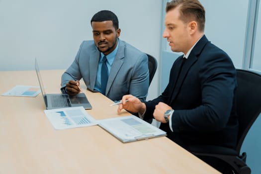 African male leader explain strategy while show solution to professional project manager by pointing at document, using laptop. Skilled business team brainstorming idea. Business meeting. Ornamented.