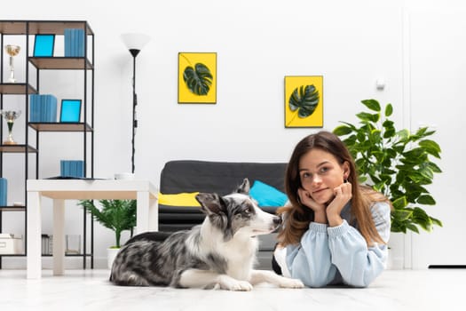 The dog sitter lies with him on the floor of the owl house in the living room and rests during a break from training. Purebred Border Collie dog in shades of white and black, and long and fine hair. Living room in a modern styling.