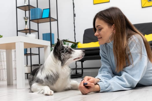 Faithful friends, dog and human, look each other in the eye while lying on the floor of the house. Purebred Border Collie dog in shades of white and black, and long and fine hair. Living room in a modern styling.