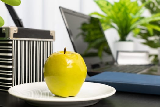 There is a green apple on the employee's desk as a vitamin dessert to be consumed during a break from work. Computer workstation for remote work with a tasty incentive.