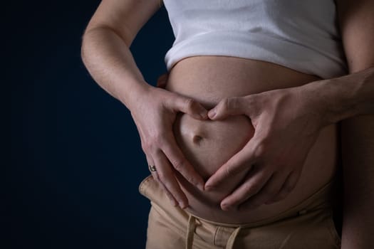 The husband and wife placed their hands in the shape of a heart on a large pregnancy belly. Symbol of love. Unborn baby in the belly.