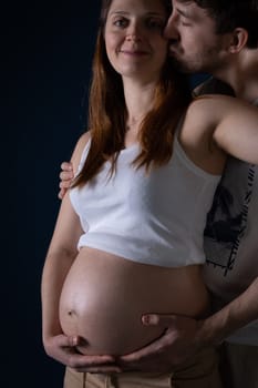 A love kiss from a husband to his wife. The woman smiles gently. Ninth month of pregnancy. Unborn baby in the belly.