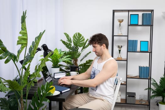 A relaxed employee is at home sitting at the computer typing on the laptop keyboard. Remote work during a pandemic. A bright living room in a modern style with a preferable space.