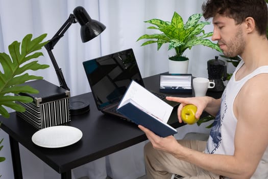 Sitting at the desk at home, the employee checks the entries in the book calendar to know where to start work. Remote work during a pandemic. A bright living room in a modern style with a preferable space.