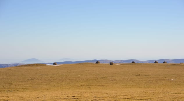 Panoramic view of hay bales in a farmer's field against a clear mountain sky.