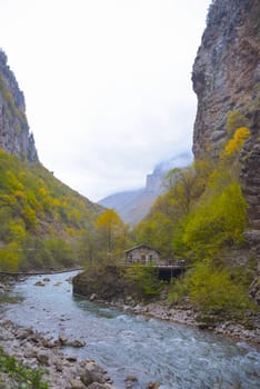 A small house near a mountain river and the foot of the misty mountains. North Caucasus, Russia
