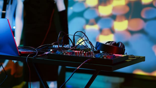 Empty DJ mixing panel at funky club, spotlights and disco ball at the bar used for dancing and clubbing. Dance floor at discotheque with audio equipment station used for partying, nightlife.