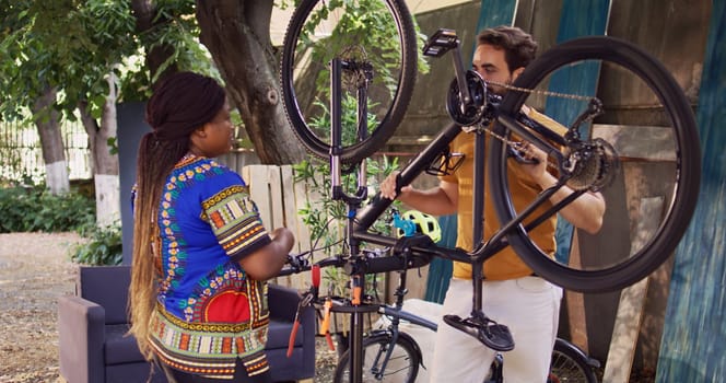 Girlfriend and boyfriend fixing bike tire with specialised tools in home yard as yearly maintenance. Athletic interracial couple discussing on best way to repair and maintain bicycle.